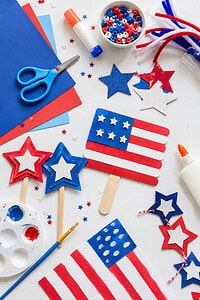 red, white, and blue themed materials such as construction paper, star-shaped cutouts, child-safe scissors, glue sticks, paint brushes, popsicle sticks, and small DIY craft projects (like paper flags or star garlands).