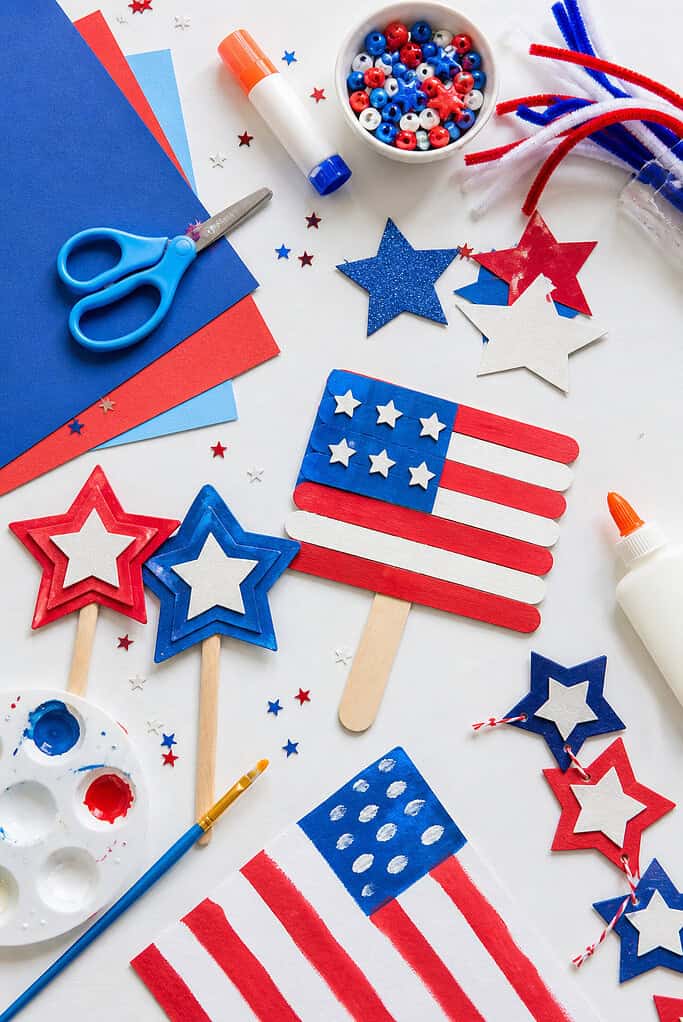 red, white, and blue themed materials such as construction paper, star-shaped cutouts, child-safe scissors, glue sticks, paint brushes, popsicle sticks, and small DIY craft projects (like paper flags or star garlands).