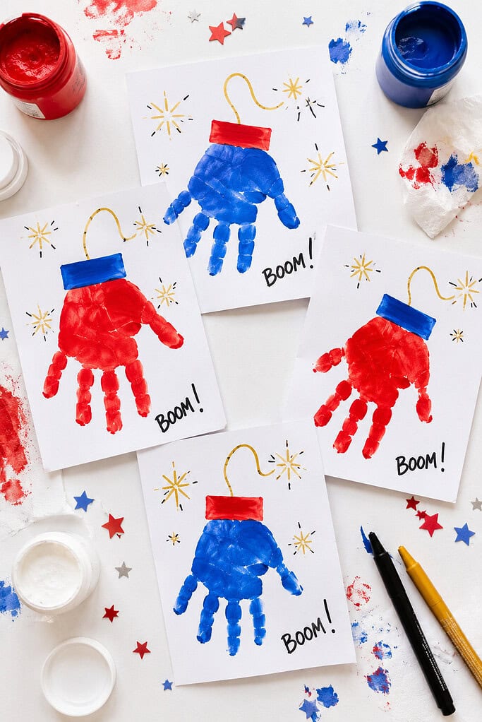 white cardstock cards decorated with red, white, and blue toddler handprints transformed into firecrackers