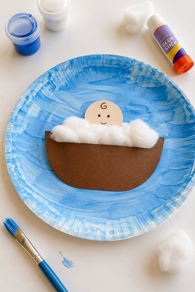 a simple brown cardstock basket shape (no weaving or complex detail). Inside the basket, a small baby figure made from basic shapes peeks out, with only the head visible.