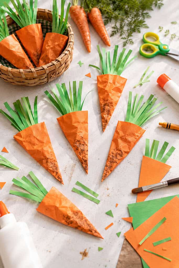 several handmade carrot crafts created from orange cardstock triangles with feathery green paper tops made from thin construction paper strips