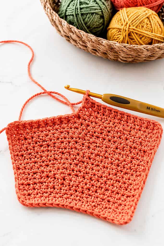 a partially completed crochet dishcloth made with textured 100% cotton yarn using simple single crochet or double crochet stitches.