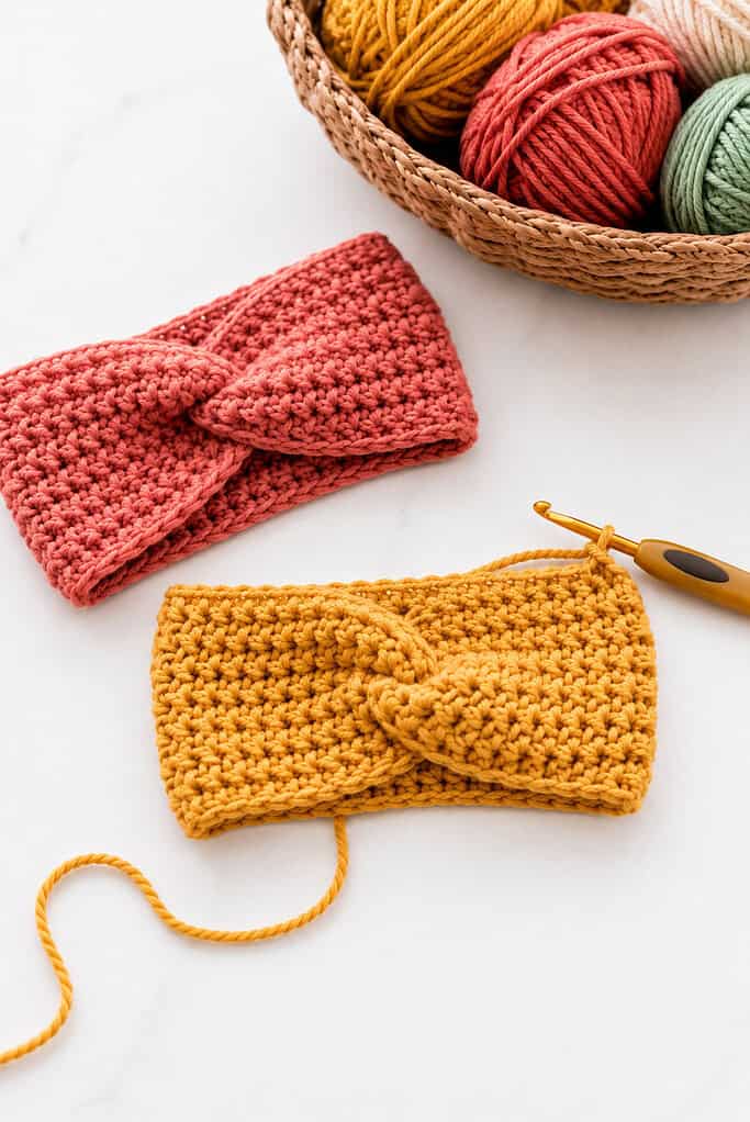 a cozy crocheted headband made with chunky or worsted-weight yarn in warm vibrant colors such as mustard yellow, terracotta, sage green, dusty rose, cream, or soft turquoise