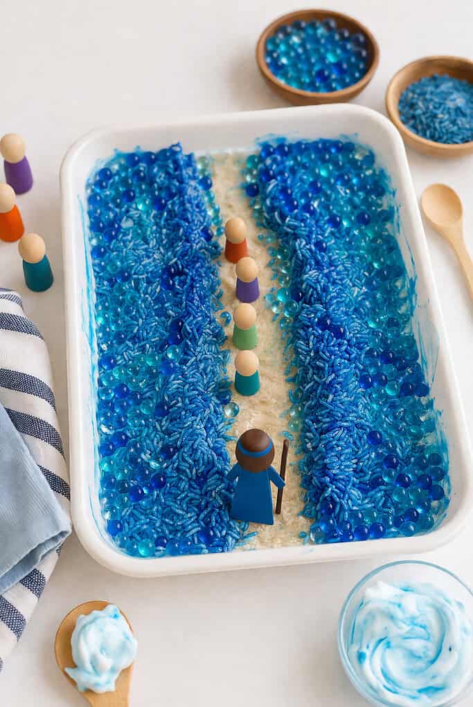 a shallow sensory tray filled with blue materials representing the Red Sea—such as glossy blue water beads, dyed blue rice, or soft swirls of shaving cream