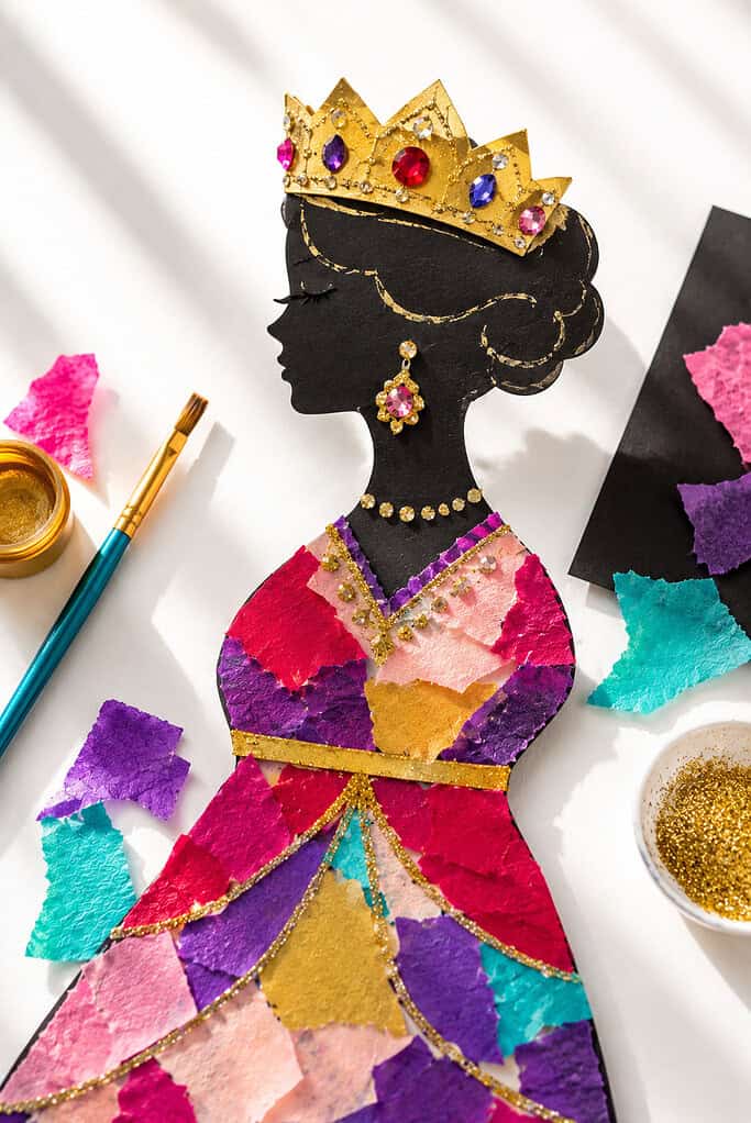 a simple queen silhouette cut from black cardstock as the main focal point, decorated with gold paint, glitter glue, and colorful torn tissue paper pieces forming a royal dress and crown