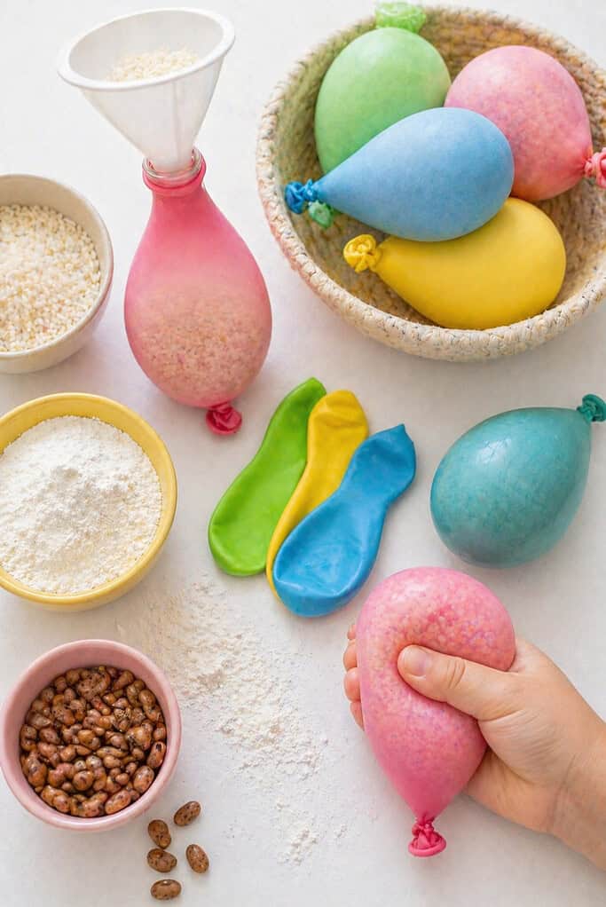 a funnel inserted into a balloon, small bowls or piles of filling materials like flour, rice, and dried beans, and a few unfilled balloons nearby