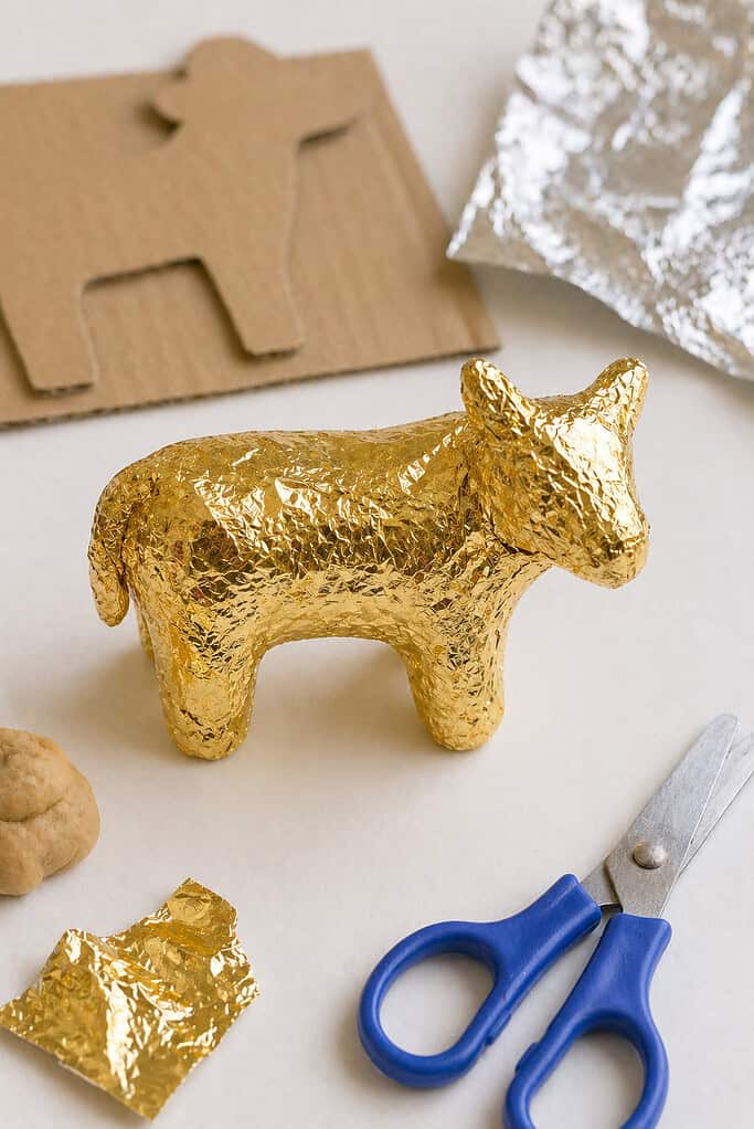 a small handmade golden calf figure created from a simple base (cardboard cutout or a small molded playdough form) fully wrapped in slightly crinkled aluminum foil.