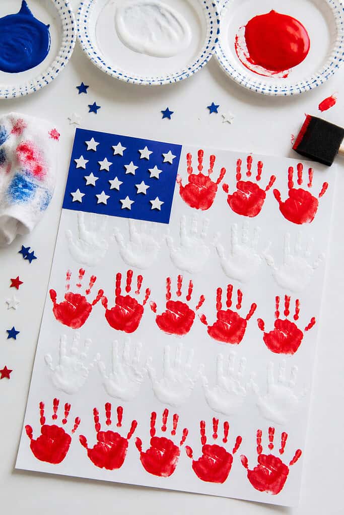 A handmade American flag created using small child handprints stamped in alternating red and white stripes across a sheet of white cardstock.