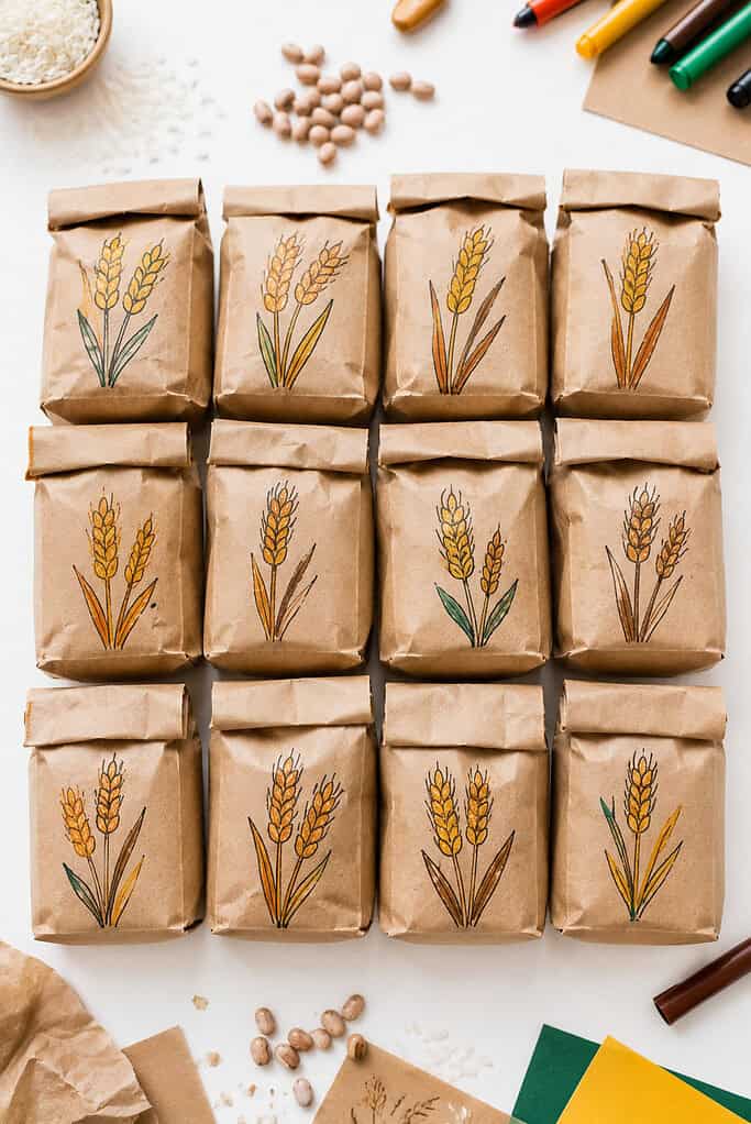 simple handmade “grain sacks” created from small brown paper lunch bags filled with dried beans, rice, or crumpled paper and lined up neatly on a bright white tabletop.