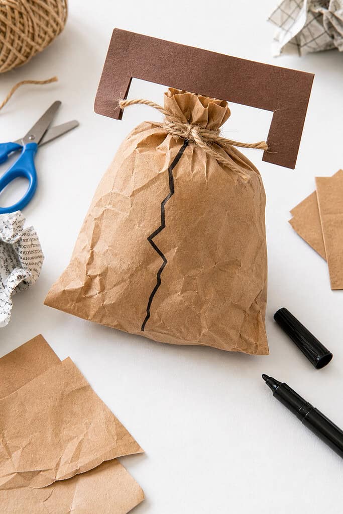 A handmade Liberty Bell created from a small brown paper lunch bag, gently stuffed with crumpled newspaper to give it a rounded, bell-like shape.