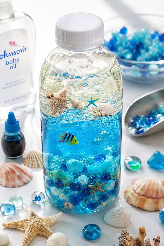one clear plastic bottle as the main focus, filled halfway with vibrant blue-tinted water and topped with translucent baby oil