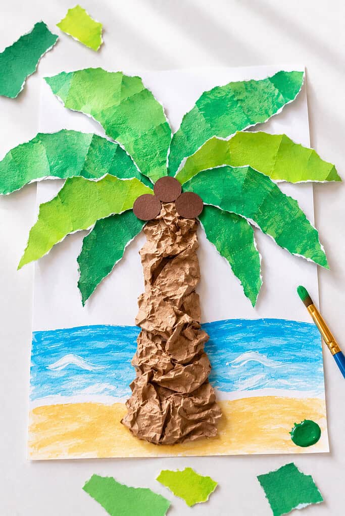 A playful handmade palm tree craft with a textured trunk made from twisted and scrunched brown paper bags attached to a painted or cardstock base.