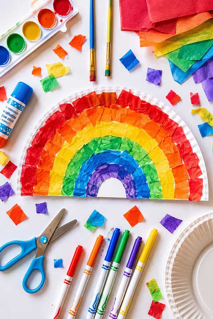 A paper plate cut in half and decorated into a rainbow using bright red, orange, yellow, green, blue, and purple tissue paper pieces.