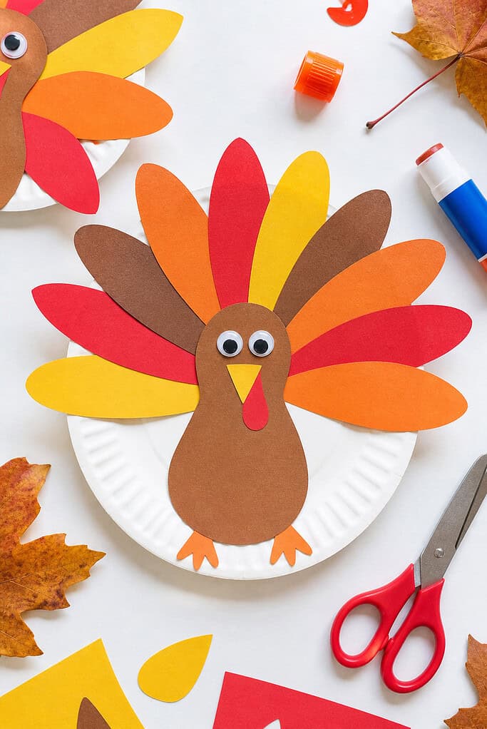 A white paper plate transformed into a turkey, with colorful construction paper feathers arranged in a fan around the rim