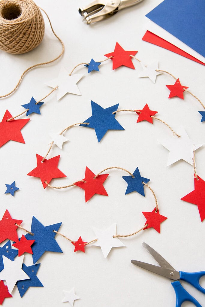 A handmade garland made of star-shaped cutouts in three different sizes, crafted from red, white, and blue cardstock.