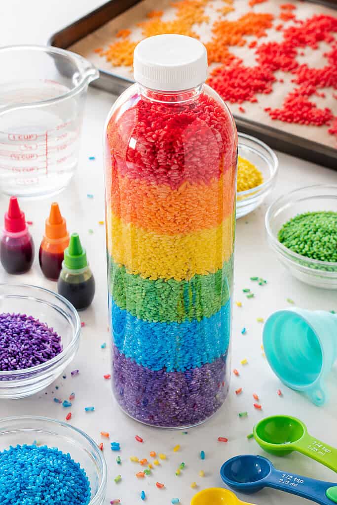 one tall clear plastic bottle filled with perfectly layered rainbow-colored rice in vivid stripes of red, orange, yellow, green, blue, and purple.