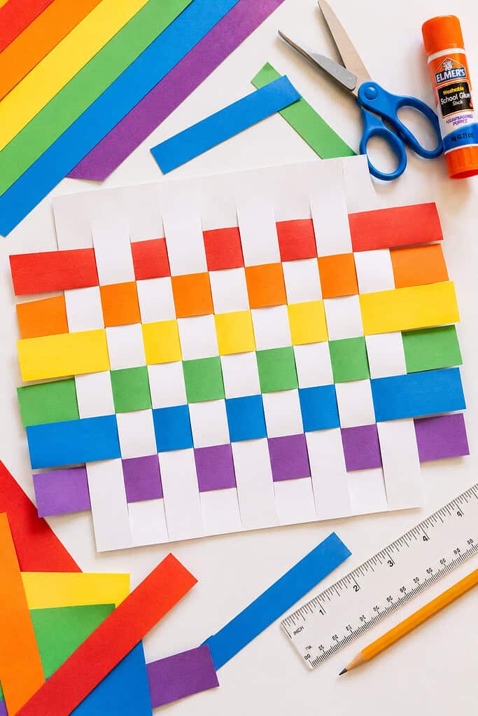 A woven paper project using vibrant strips of red, orange, yellow, green, blue, and violet paper threaded through carefully cut slits in white cardstock.