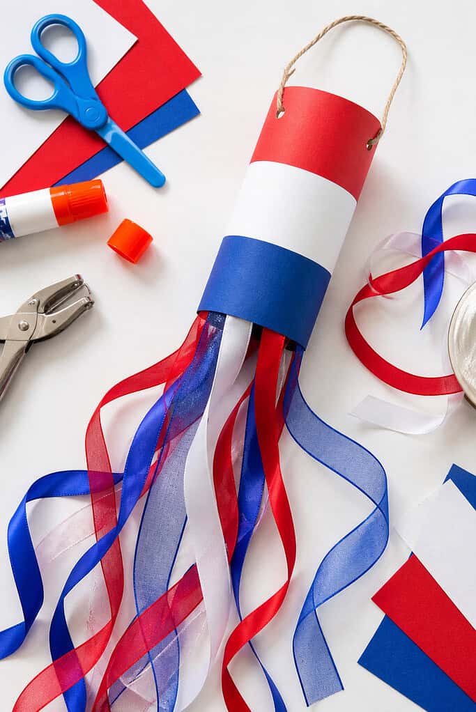 A handmade windsock created from a cardboard toilet paper roll wrapped neatly in red, white, and blue construction paper.