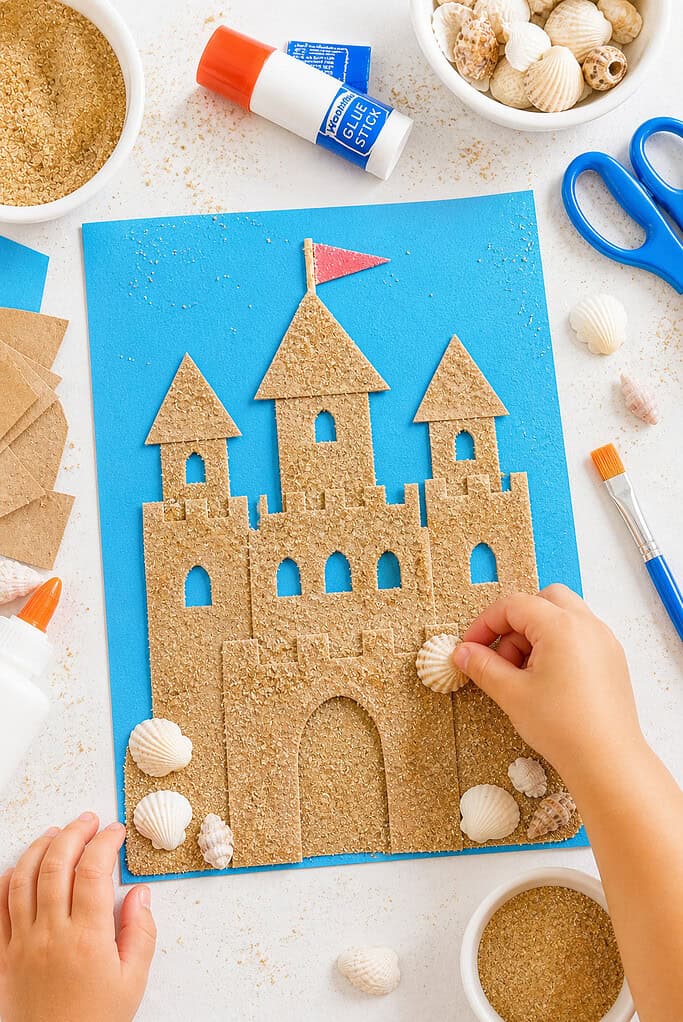 a handmade sand castle collage created from cut pieces of brown paper grocery bag material glued onto vibrant blue cardstock
