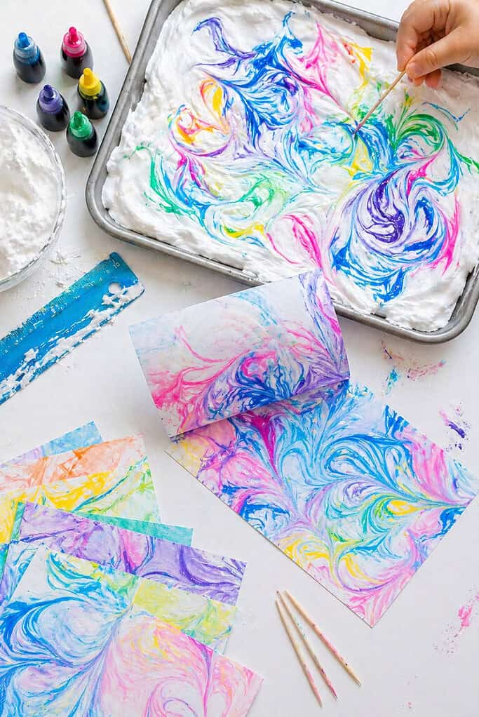 a shallow baking tray spread with a thick, even layer of shaving cream, with drops of vibrant food