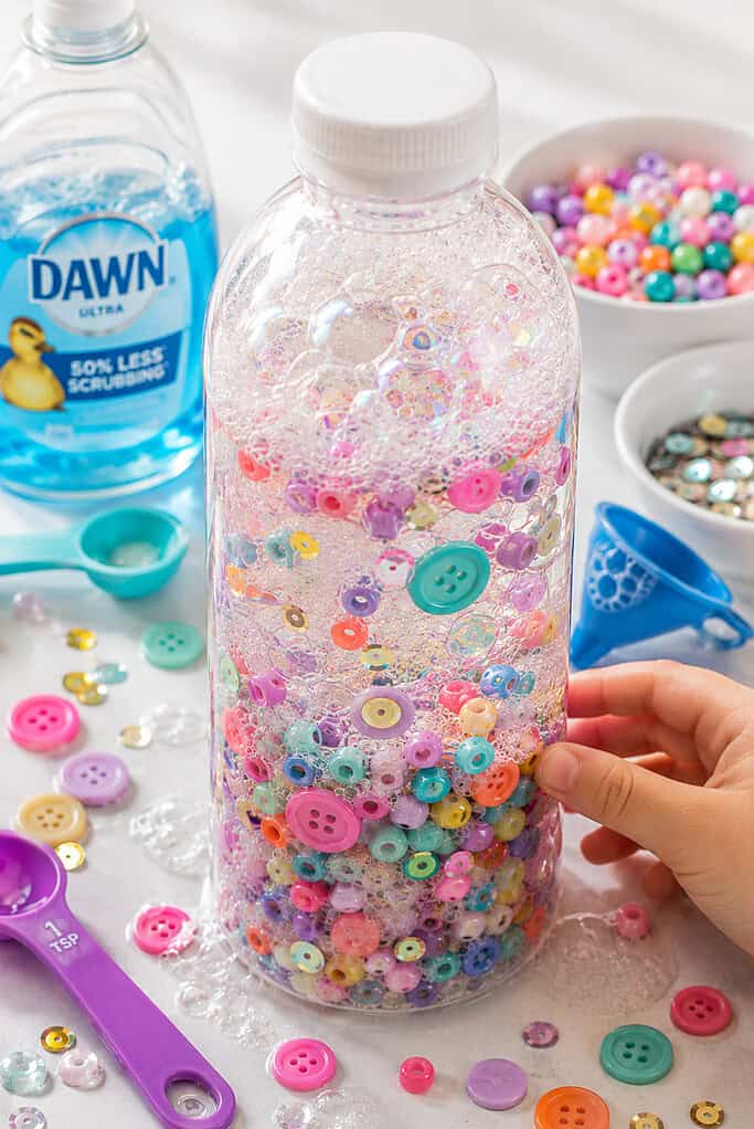 one clear plastic sensory bottle  filled mostly with warm soapy water creating soft foamy bubbles and delicate swirling suds
