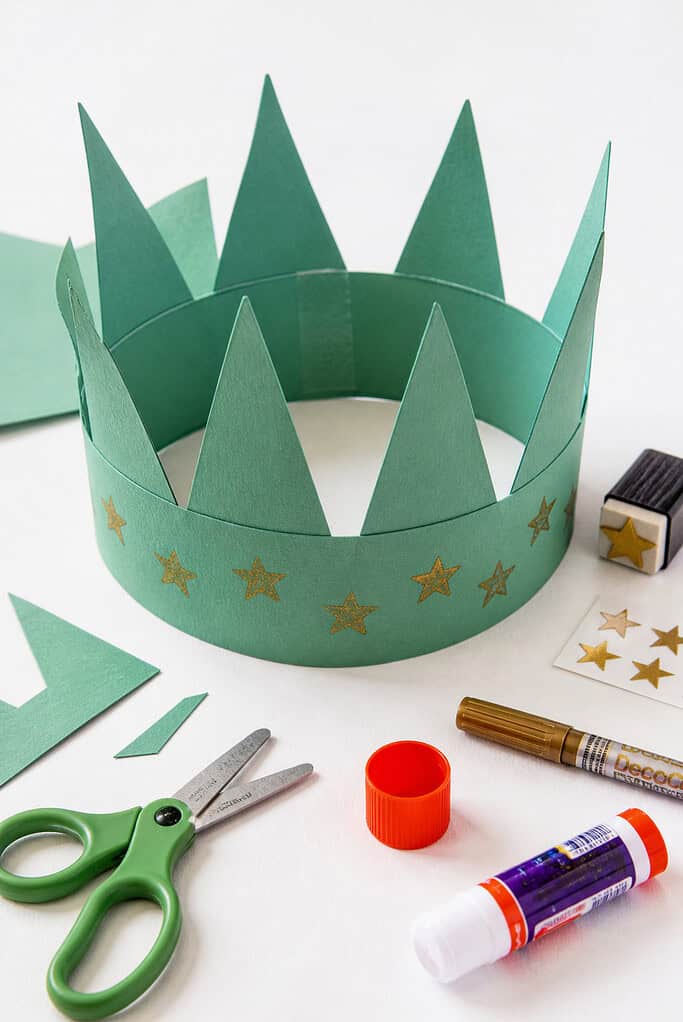 A handmade crown created from a strip of green construction paper, formed into a circle with seven triangular points cut along the top edge to resemble the Statue of Liberty’s crown.