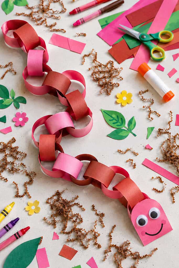 an extra-long paper chain worm made from alternating loops of pink and reddish-brown construction paper strips linked together into a winding worm shape