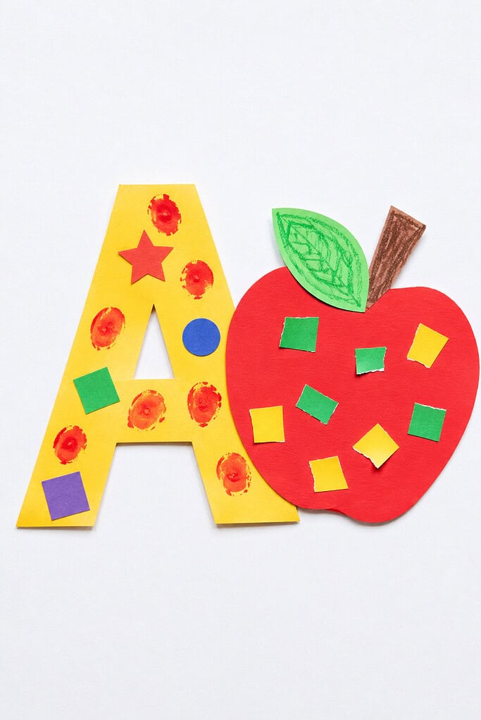 A large yellow foam letter A decorated with colorful stickers and painted dots, next to a red foam apple shape with a brown stem, green leaf, and colorful square stickers