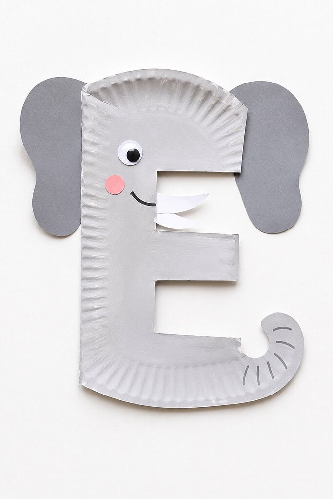 Gray paper plate cut into the letter E shape with three horizontal prongs, two large gray rounded ears attached on either side, a single googly eye, a small pink circle cheek, and a curled gray trunk at the bottom right