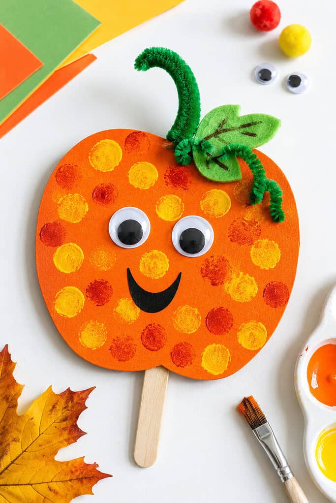 Handmade pumpkin crafts created from vibrant materials such as orange cardstock, colored paper, felt, pipe cleaners, pom-poms, googly eyes, paint, and craft sticks.