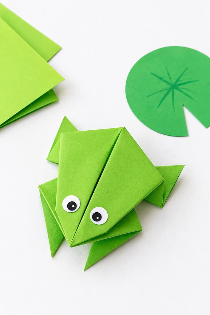 a carefully folded frog made from bright green origami paper, designed in the classic jumping frog style with folded legs and body that allow it to hop when pressed.