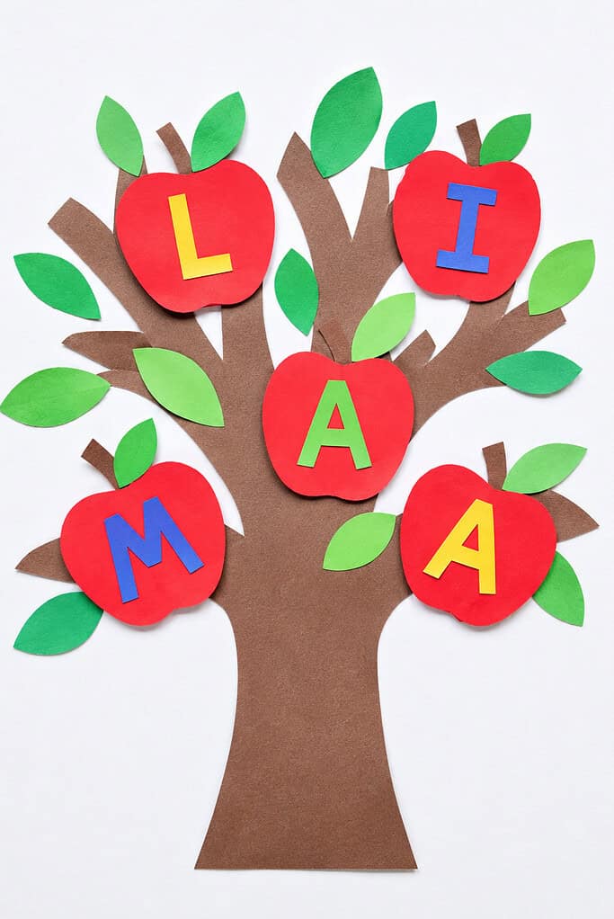 A brown paper tree with green leaves and five red paper apple shapes in the branches, each displaying a single colorful letter