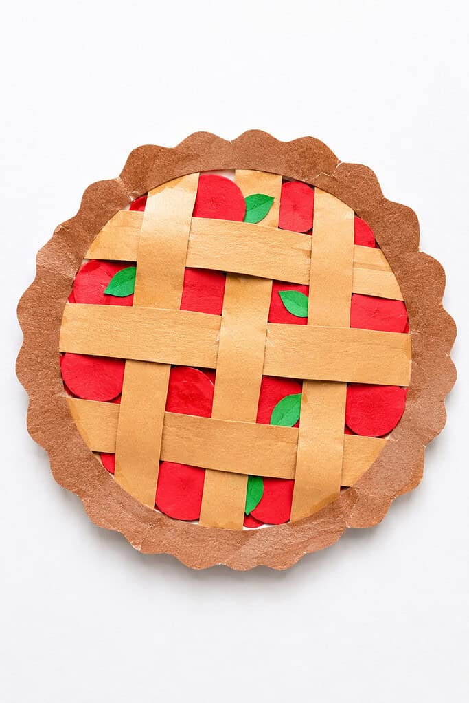 A paper pie with a scalloped brown crust border and tan paper strips woven in a lattice pattern over a red and green paper filling