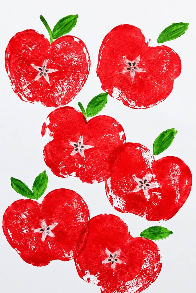 Multiple red apple-shaped stamps on white paper, each showing a star-shaped core pattern in the center with green painted leaves