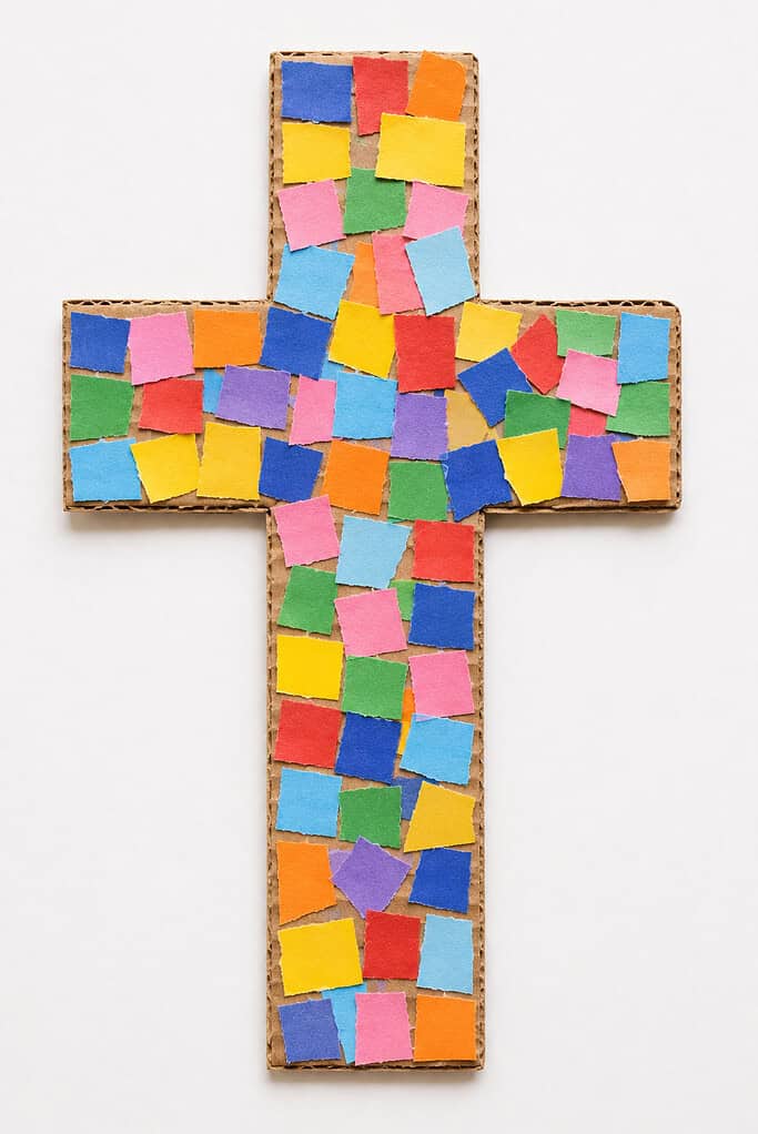 A cardboard cross covered with small squares of torn colored paper in blue, red, yellow, green, orange, and purple arranged in a mosaic pattern