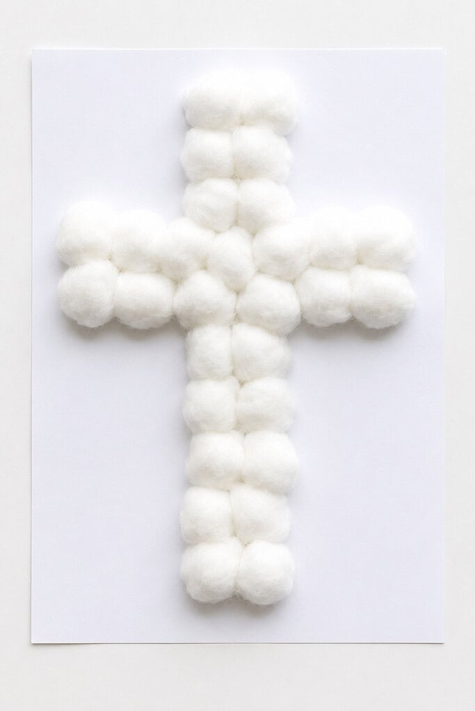 White cotton balls arranged in the shape of a cross on a white sheet of paper