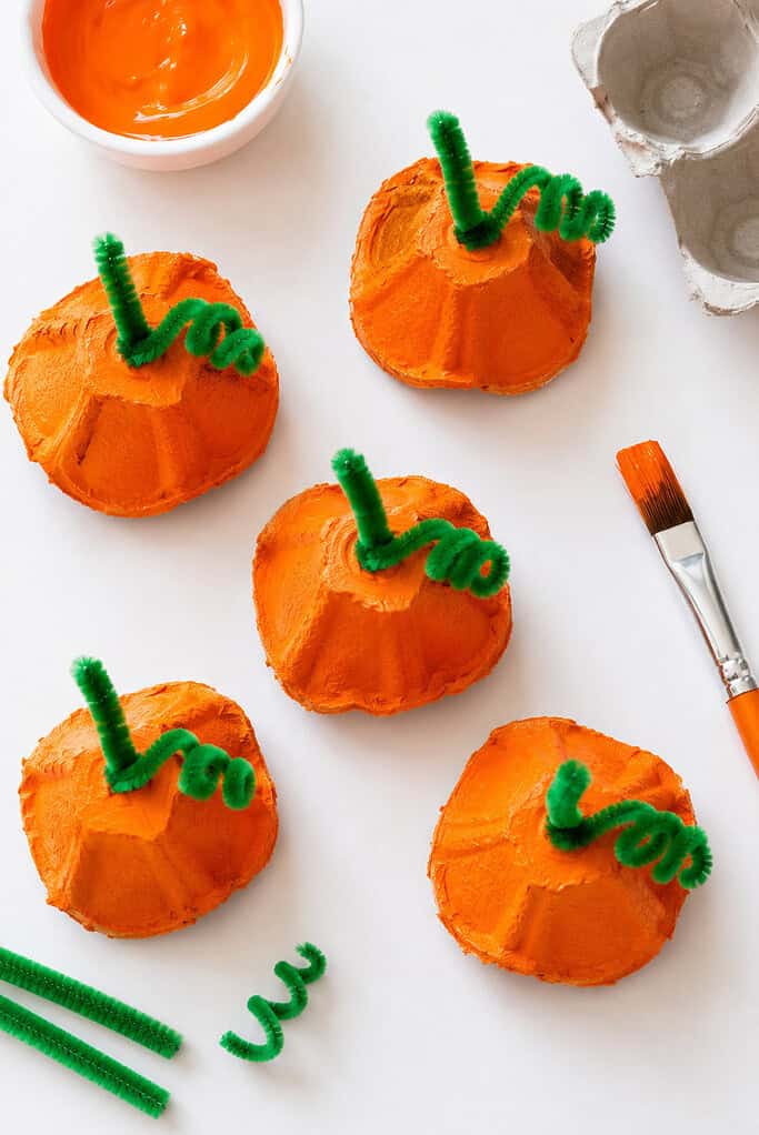 Several handmade pumpkins created from recycled egg carton cups that have been cut out, painted a vibrant orange, and transformed into miniature pumpkins.