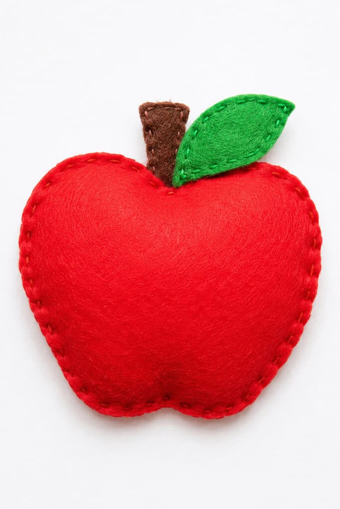 A puffy red felt apple shape with visible stitching around the edge, a brown felt stem, and a green felt leaf