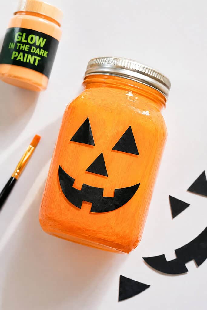 A clean glass jar transformed into a pumpkin lantern by painting the inside with vibrant glow-in-the-dark orange paint.