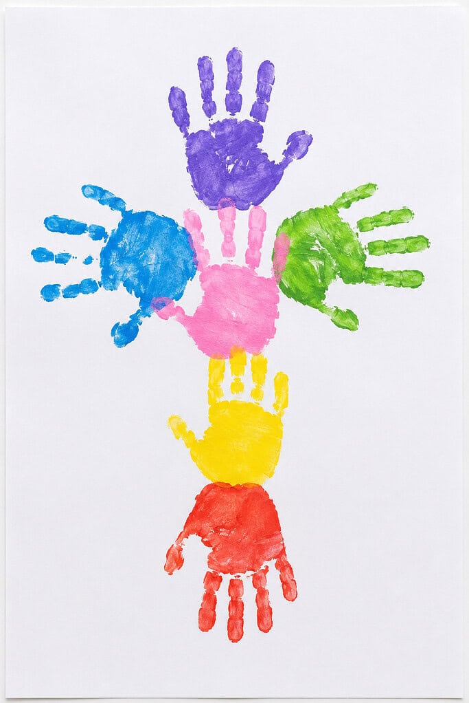 Colorful painted handprints arranged in a cross pattern on white paper, with purple at the top, blue and green on the sides, pink in the middle, and yellow and red below