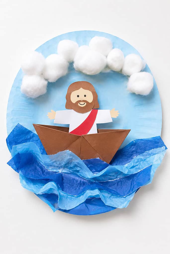 a small handmade paper boat floating on layered blue tissue-paper waves. Inside the boat is a simple child-friendly paper Jesus figure with a warm smile.
