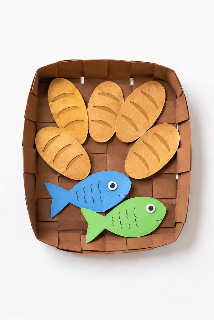 a small handmade basket created from woven paper strips or simple brown cardstock, holding exactly five tiny paper loaves of bread and two colorful paper fish.