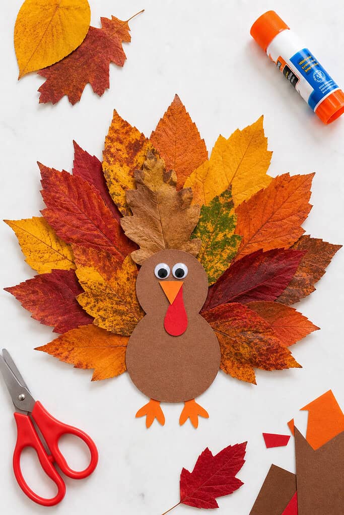 A child-created leaf collage displayed on a sheet of white cardstock.