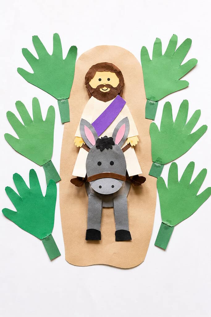 several green handprint palm branches cut from construction paper and arranged along both sides of a simple paper road. A small paper donkey carries a handmade paper Jesus figure down the center path.