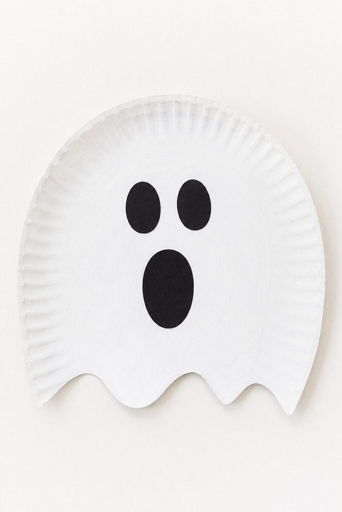 A white paper plate cut into a ghost shape with a wavy bottom edge, with two black oval eyes and a black oval open mouth glued on