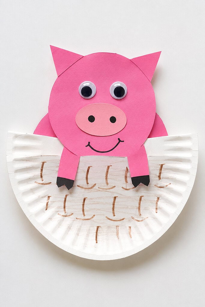 a white paper plate folded in half to create a simple basket or pocket shape. Tucked inside the folded paper plate is a cheerful pink paper pig made from basic cut shapes.