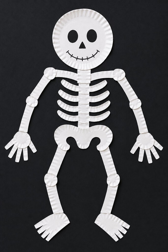 A full-body skeleton assembled from cut paper plates, with a round head with drawn oval eyes and a stitched smile, a ribcage torso, and paper strip arms and legs with small paper hands and feet, displayed on a dark background