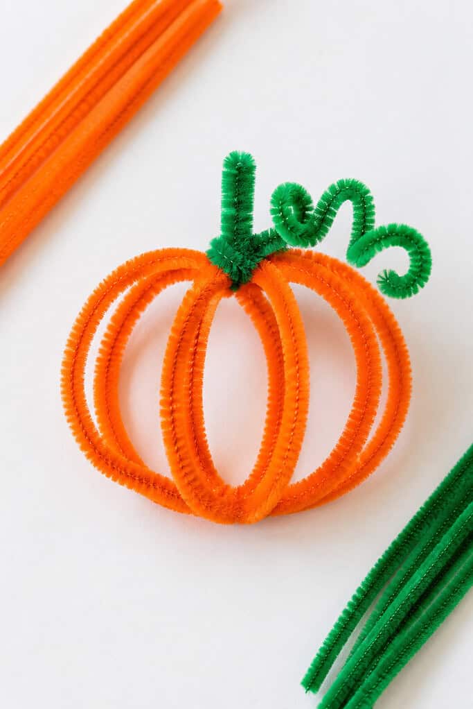 A handmade pumpkin created from several vibrant orange pipe cleaners bent into a soft, rounded pumpkin shape.