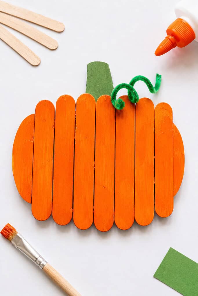 A handmade pumpkin created from several wooden popsicle sticks glued side by side and painted a vibrant pumpkin orange.