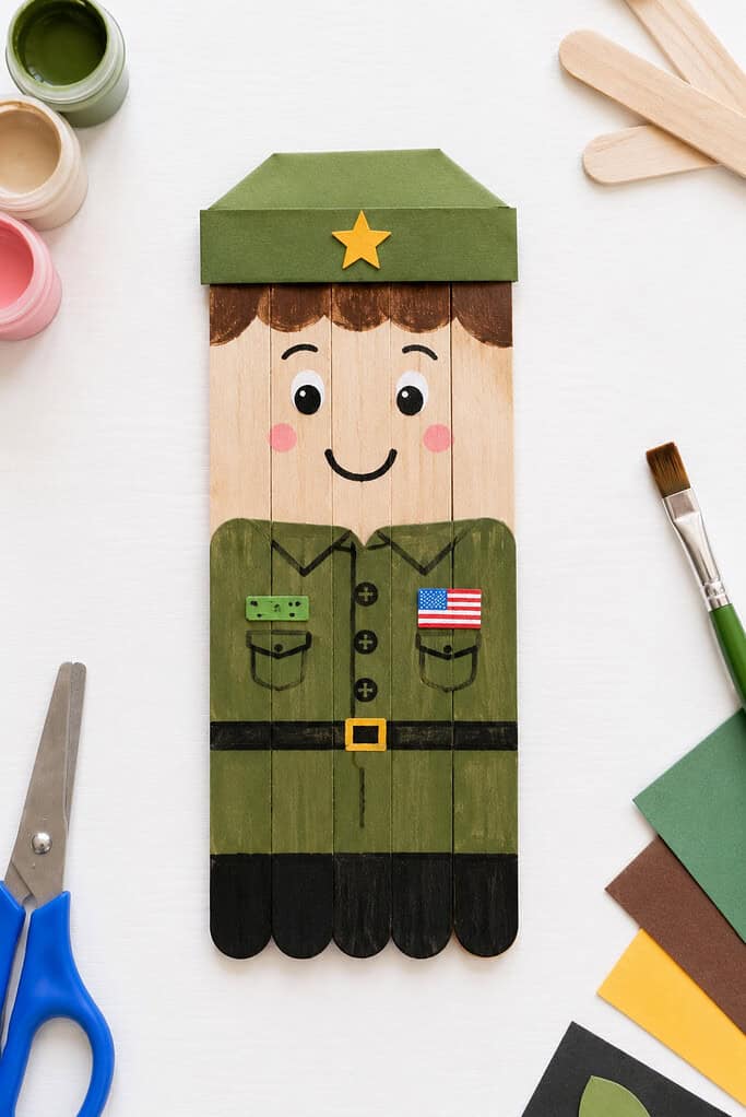 a friendly soldier figure made from several glued-together wooden craft sticks, decorated with paint and simple paper details.